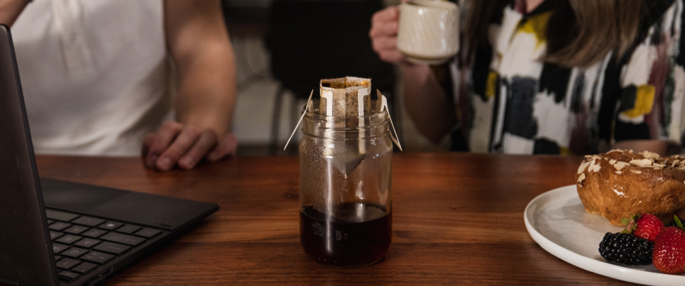 An elegantly designed Hooked Coffee pour-over coffee package in a glass jar, rests on a rustic wooden table